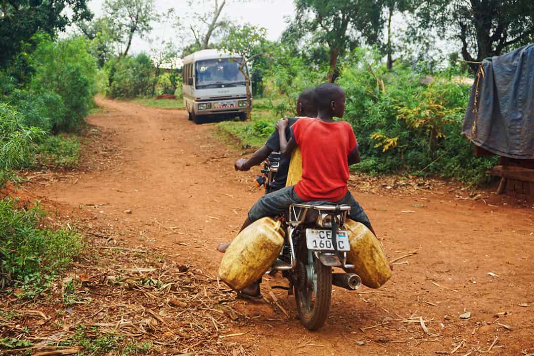 People riding a motorcycle on a dirt road in Uganda. Photo by Melissa Askew